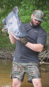 Man holding catfish in water werting shorts